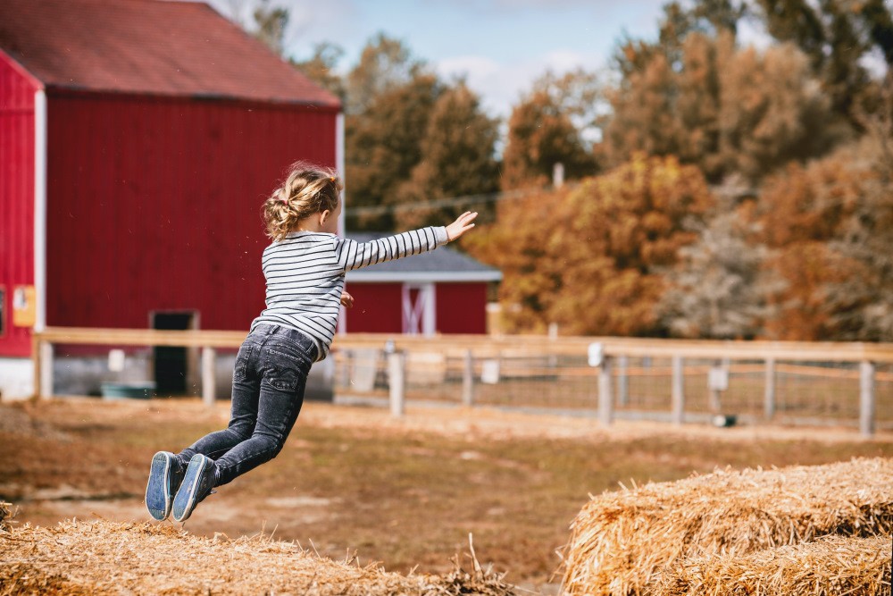 child jumping off a barrel of hay